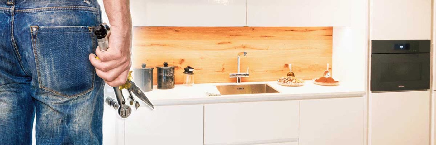 Monteur mit Werkzeug vor einer weißen Küchenzeile mit Holzrückwand