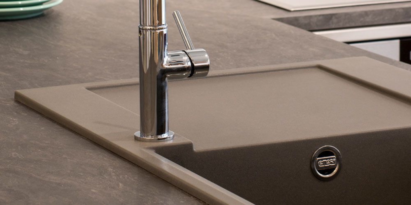Detailaufnahme einer neuen Spüle mit Armatur in einer dunklen Arbeitsplatte